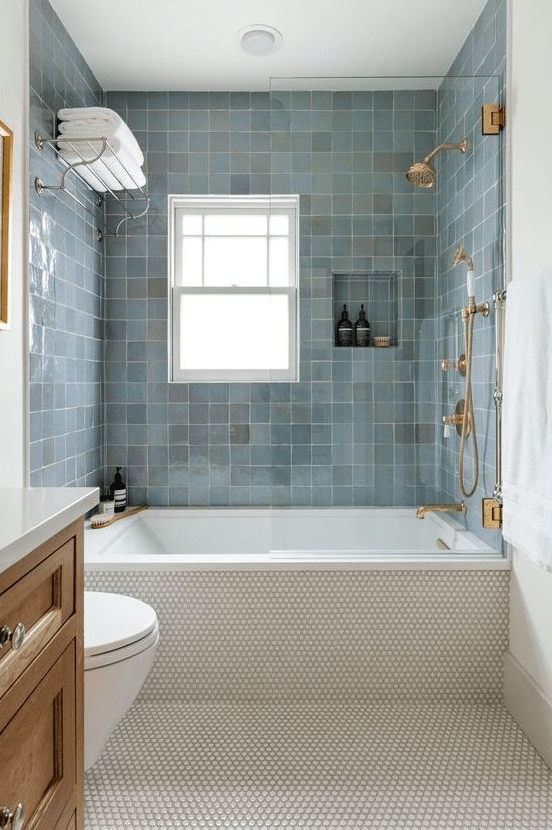 a modern bathroom with penny tiles and blue zellige tiles around the bathtub, a wooden vanity and gold and brass fixtures