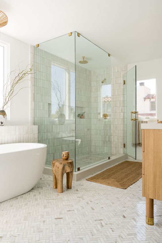 a calm, modern bathroom with marble and zellige tiles, a shower and bathtub, a stained vanity and a wooden stool