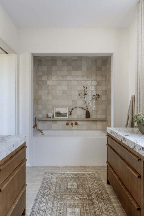 a neutral, organic bathroom with a built-in soaking tub in a zellige tile-lined alcove, richly stained vanities, and white stone countertops
