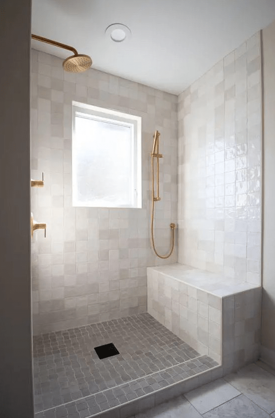 a modern neutral bathroom with neutral zellige tiles, stone tiles on the floor and brass and gold fixtures