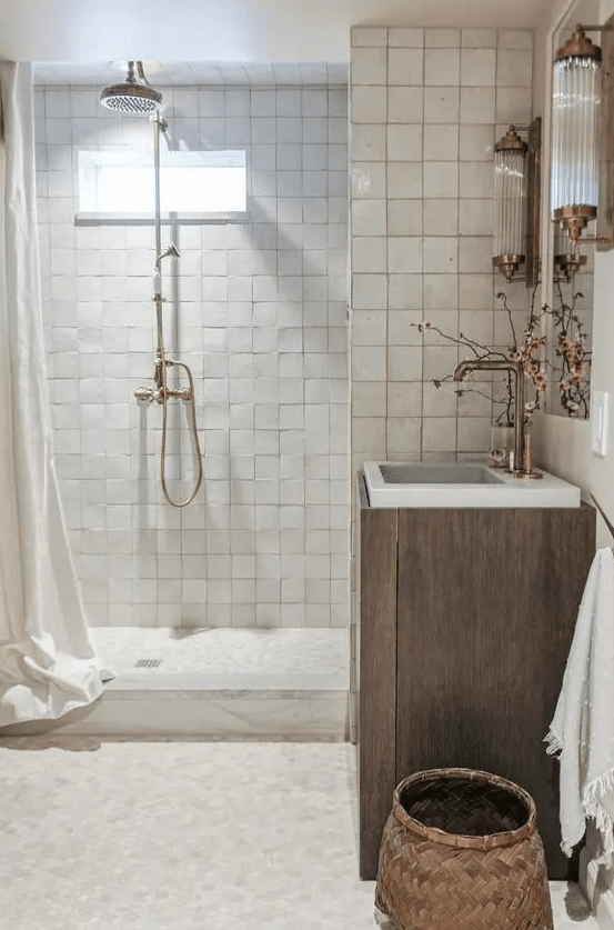 a neutral bathroom with neutral zellige tiles, a wooden vanity, a mirror, some beautiful vintage pedestals and a basket
