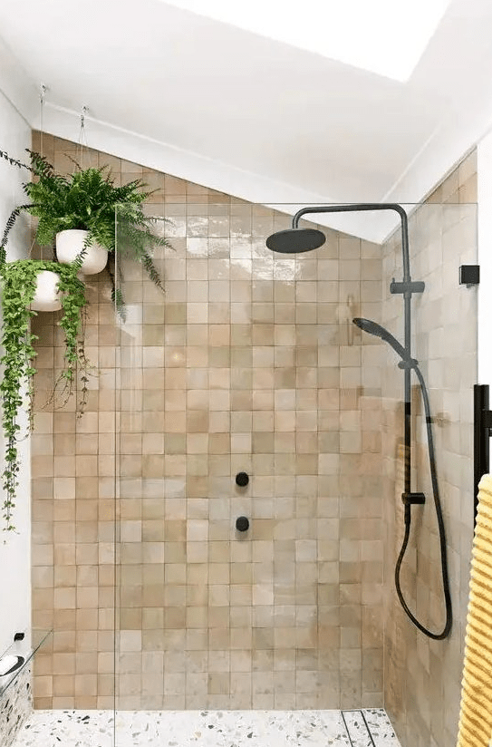 An attic shower area clad in blush and brown zellige tiles, with hanging potted plants and black fixtures for a modern feel