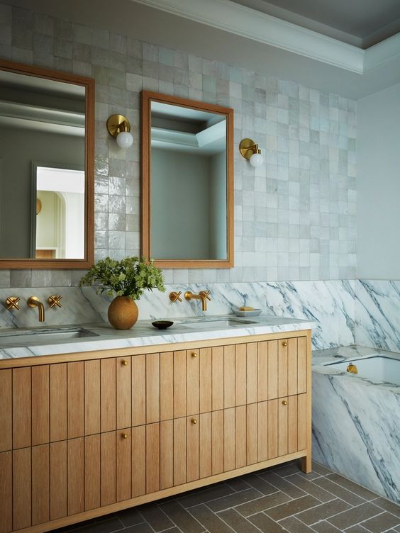 a sleek, neutral bathroom with white zellige tiles, a marble-clad tub, a stained vanity, and brass hardware and fixtures