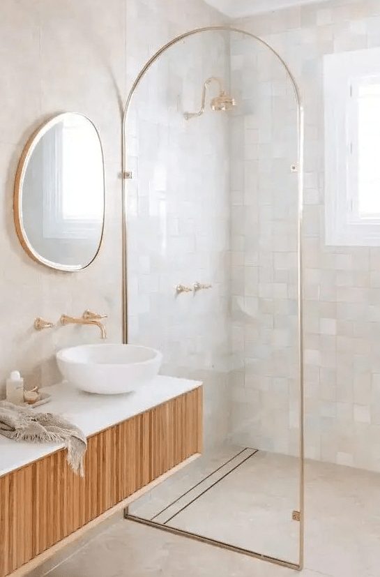 a sophisticated bathroom with neutral and pastel zellige tiles in the shower, a curved room divider and a floating wooden vanity