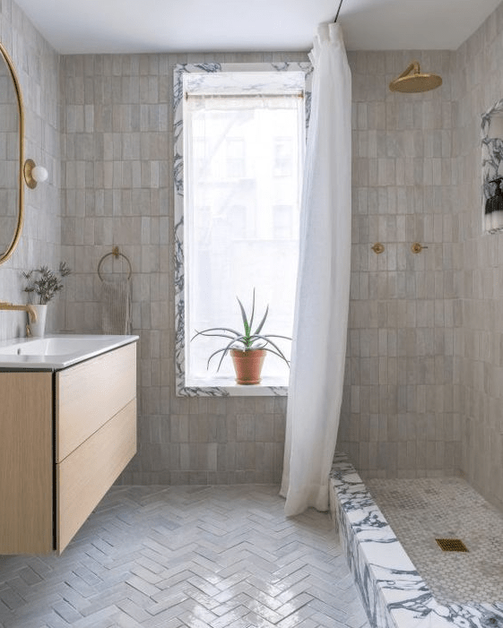 a neutral bathroom with stacked zellige and herringbone tiles, a shower, a floating vanity and gold fixtures