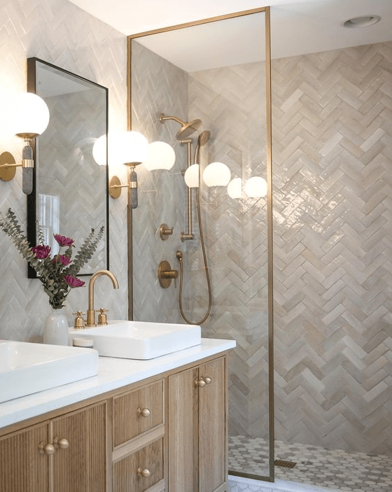 a sleek, neutral bathroom with zellige herringbone tiles, a stained vanity, sink, gold fixtures and some greenery