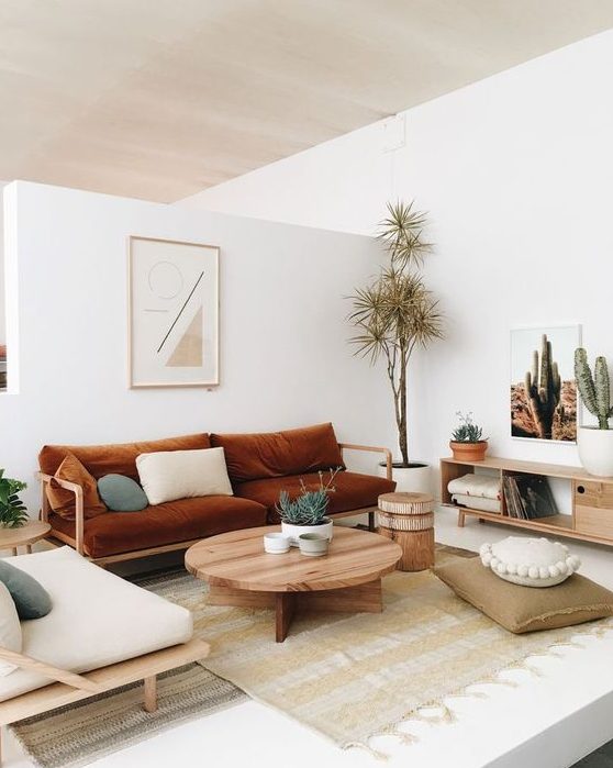 a boho living room with a rust-colored sofa, neutral furniture, a round table, simple textiles and potted plants