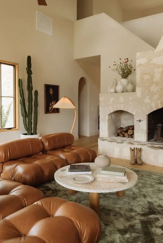 a beautiful, earthy living room with a large stone fireplace, brown leather sofa, low coffee table, green rug and plants