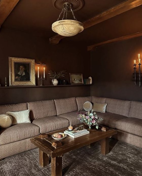 an atmospheric living room with dark brown walls, a beige sitting area, a coffee table and beautiful artwork and flowers