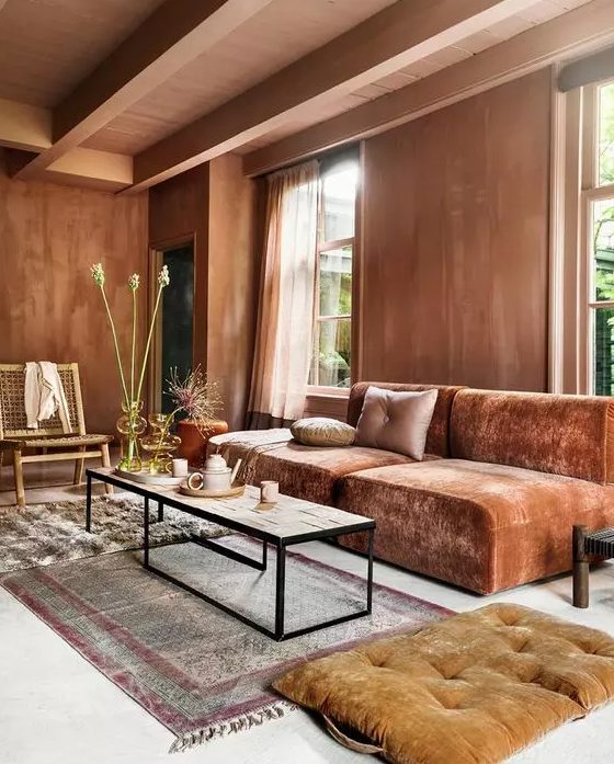 A beautiful living room with lots of texture, terracotta walls, a low burnt orange sofa, a coffee table and rust cushions