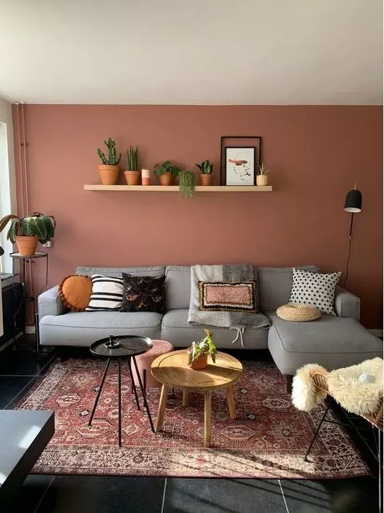 A pretty boho living room with a striking terracotta wall, a gray sofa, a rattan chair and some potted plants and round tables