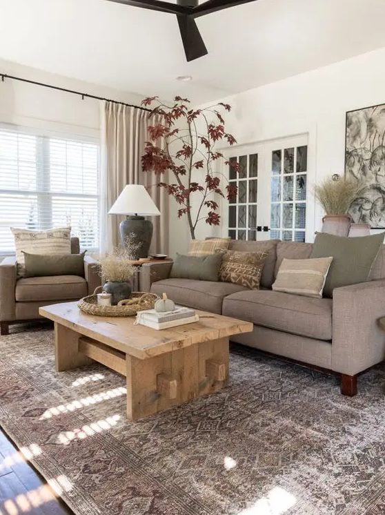 a modern, earthy living room with gray seating, a low wooden table, a printed rug, earthy cushions and potted plants