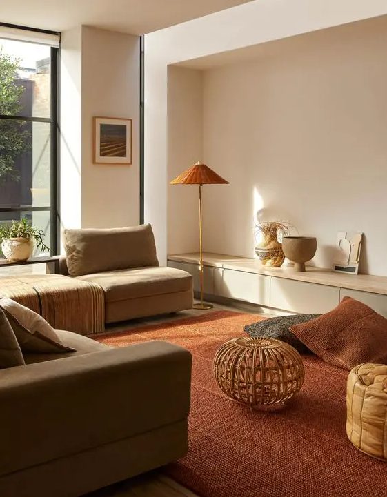 a modern, warm, earthy living room with a gray sofa and neutral seats, a deep red rug and cushions, a floor lamp and an amber stool