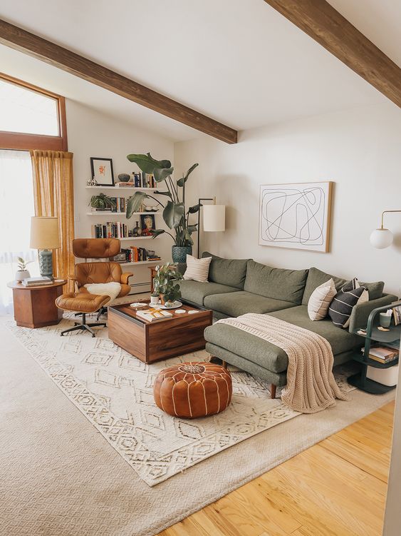a lovely earthy living room with a green sitting area, a stained table, an amber chair and a brown stool and some bookshelves