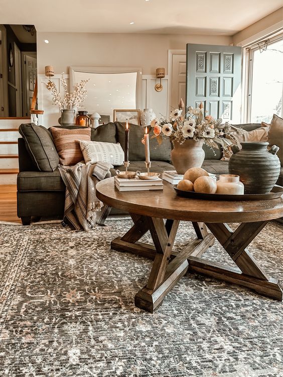 an inviting earth-toned living room with a gray sofa and earthy cushions, a printed rug, a stained round table and some candles