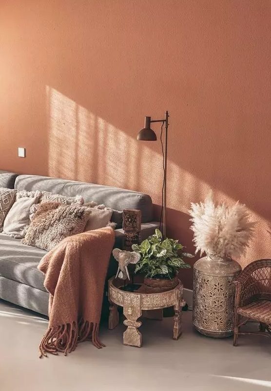 An inviting boho living room with a terracotta accent wall, a gray sofa with pillows, a carved boho side table, pampas grass and a floor lamp