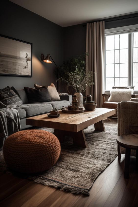 an earthy living room with gray walls, a gray sofa, a stained coffee table, leather armchairs and rusty knit stools