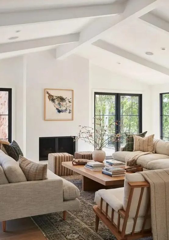 an airy living room with gray sofas, a low coffee table, a cream chair and striped stools, and a fireplace