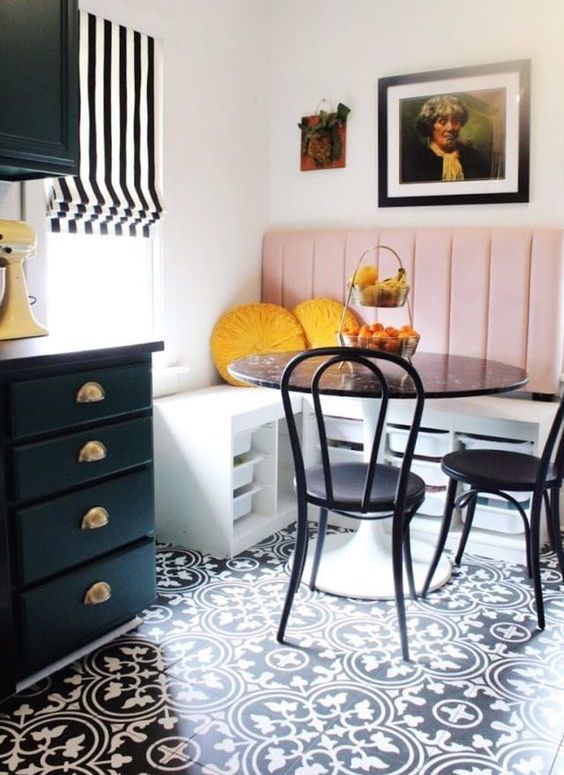 a bright breakfast nook with a corner bench with a pink backrest, a black table and chairs and a gallery wall