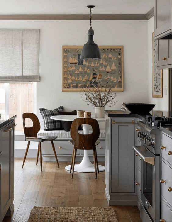 a cool, modern farmhouse kitchen with gray cabinets, black countertops, a corner dining area with a bench and a white table and chairs