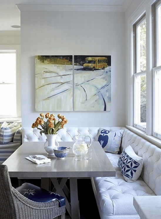 a cozy breakfast nook with a white seating area, a neutral table and wicker chairs, a mini gallery wall and some flowers