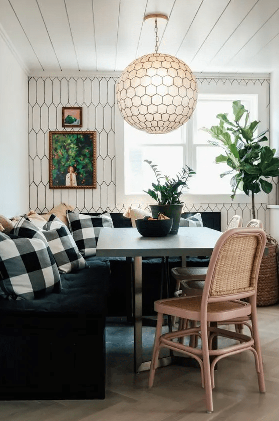 a cozy little dining nook with a black tufted bench, checkered cushions, a concrete table, woven chairs and a hexagonal pendant light