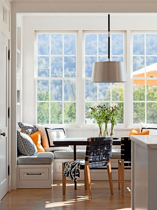 A light-filled breakfast nook with corner benches, a dark table, woven chairs and a pendant lamp is beautiful