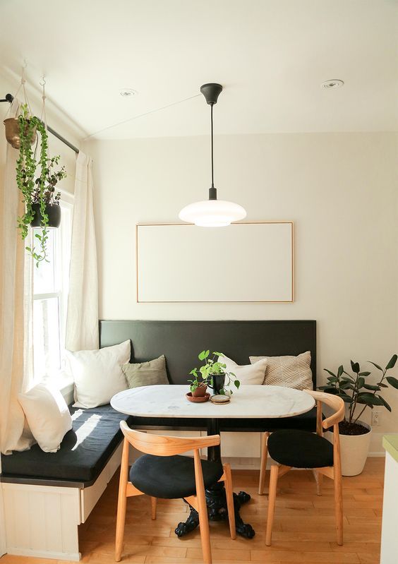 a modern breakfast nook with a black corner bench, an oval table, black chairs, potted plants and a pendant lamp