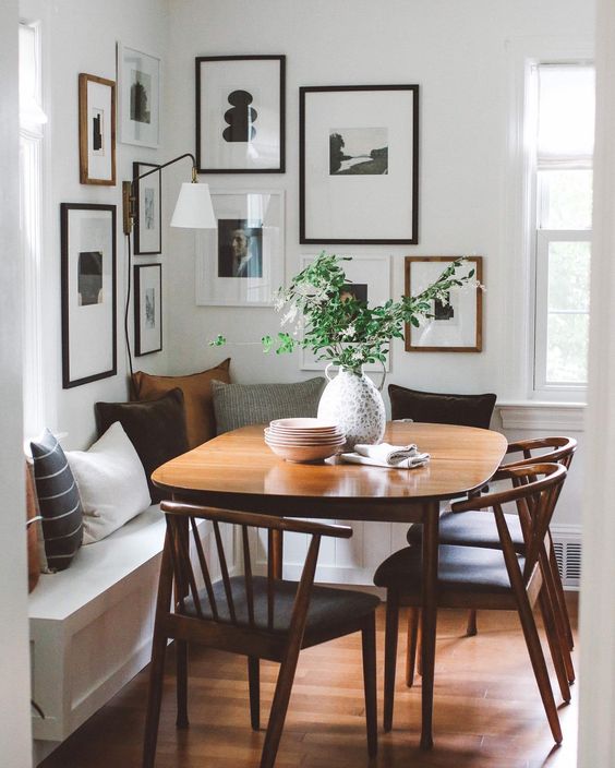 A modern farmhouse breakfast nook with a cushioned sitting area, a stained table and chairs and a cool corner gallery wall