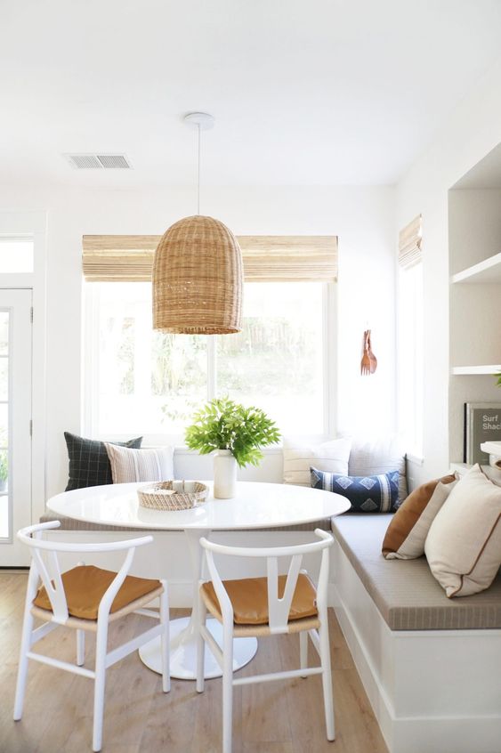 A modern, country-style breakfast nook with a seating area, a round table and white chairs, and a woven hanging lamp