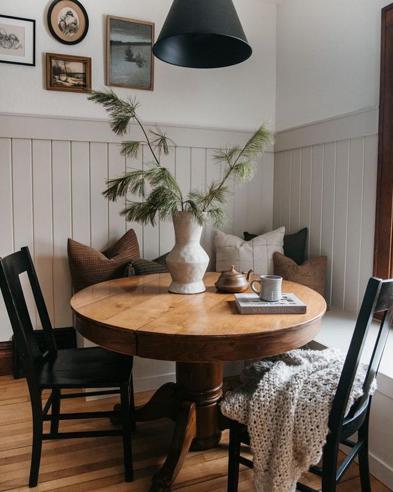 A modern farmhouse-style breakfast nook with a sitting area, a stained round table, black chairs, a black lamp and a gallery wall