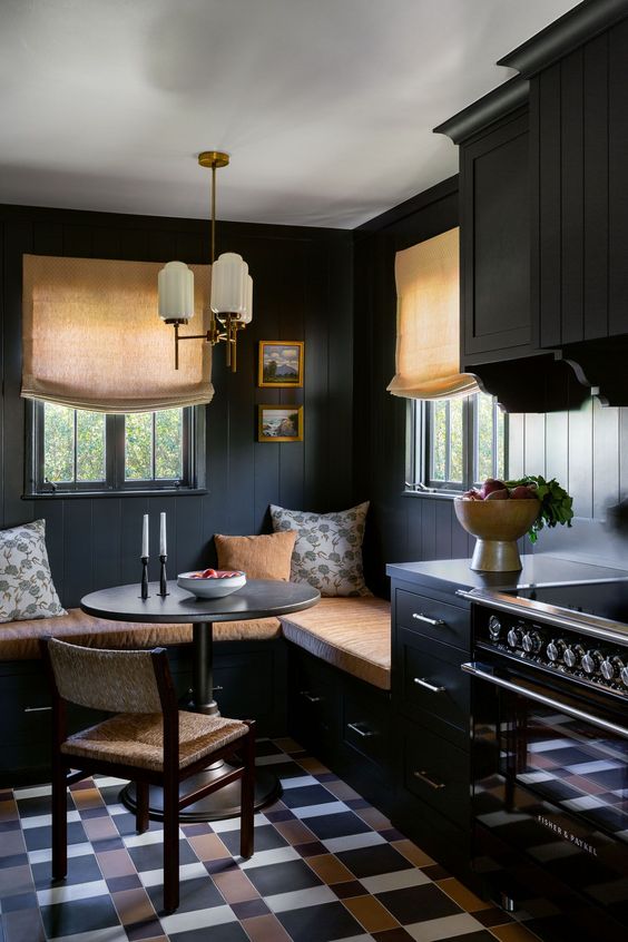 a moody black breakfast nook with corner seating and cushions, a black table and chair, a chandelier and some artwork
