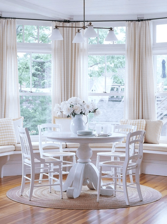 A neutral, country-style breakfast nook with white bench seating, a white table, white chairs and a chandelier