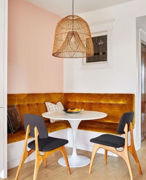 a sophisticated, modern breakfast nook with an upholstered marigold bench, round table, black chairs and a woven hanging lamp