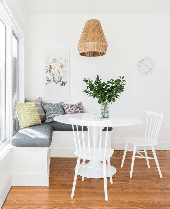 a simple and pretty breakfast nook with an upholstered bench, a round table and chairs