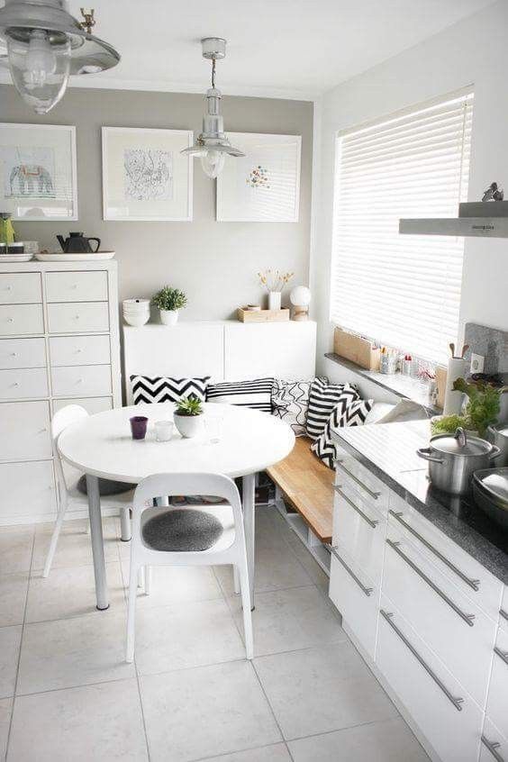 a small Scandinavian breakfast nook with corner bench and cushions, a white table and chairs and chic furnishings
