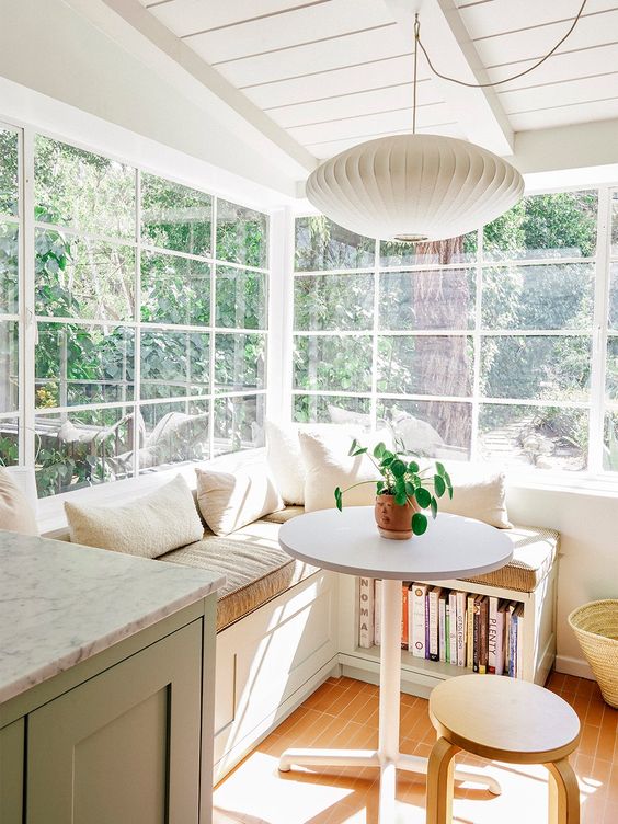 A sunny breakfast nook with a sitting area with storage, a small table and stool, and a hanging lamp is beautiful