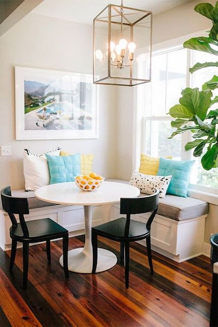 a vibrant breakfast nook with a corner bench and bright cushions, a round table, black chairs, a hanging lap and a piece of art