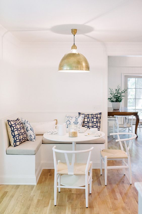 A stylish, modern breakfast nook in neutral colors with banquette seating, a round table and matching chairs, and a gold pendant lamp