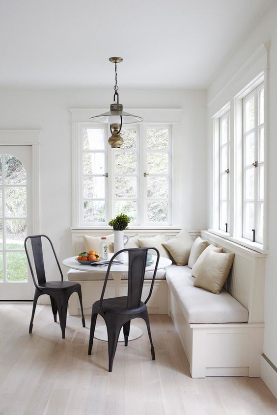 A modern, neutral breakfast nook with black chairs, a round table, lots of pillows and a vintage pendant lamp invites you to relax