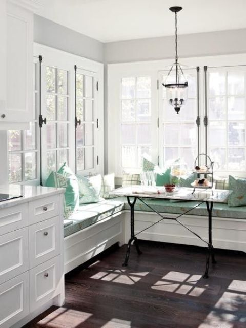 A vintage-style breakfast nook with turquoise cushions and pillows, a small black table and a pendant lamp is flooded with light