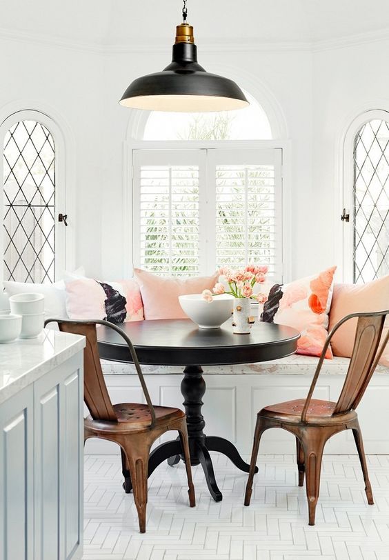 an elegant and chic breakfast nook with sophisticated bench seating and coral cushions, a black table and metal chairs, and a black pendant lamp