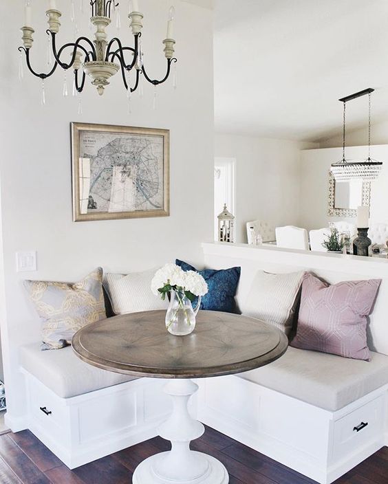 An inviting, modern, farmhouse-style compact breakfast nook with colorful pillows, a rustic-topped table and a vintage chandelier, and a map