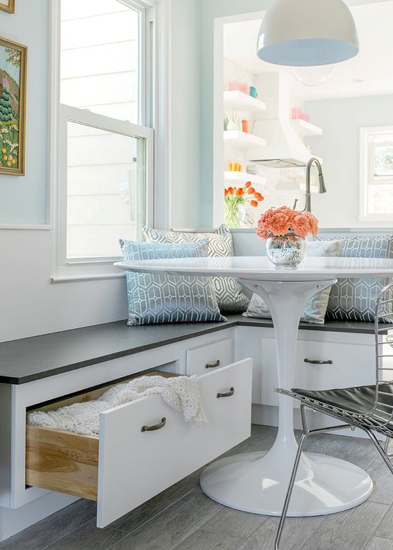 A coastal cottage style breakfast nook in shades of blue with a storage bench, a white table, metal chairs and some blue printed cushions