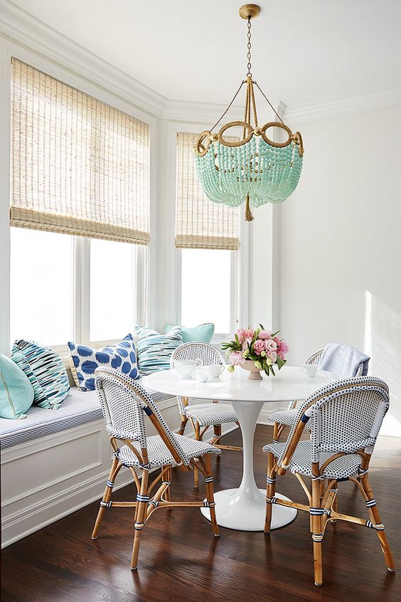 A sea blue and aqua breakfast area with rattan chairs, cushions, a turquoise beaded chandelier and woven lampshades
