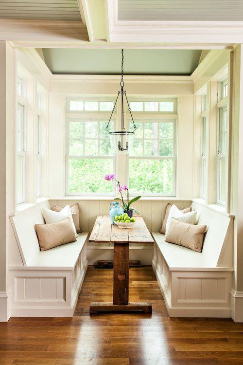 a cozy, rustic breakfast nook with a raw wood table and a U-shaped bench, a pendant lamp and some pillows