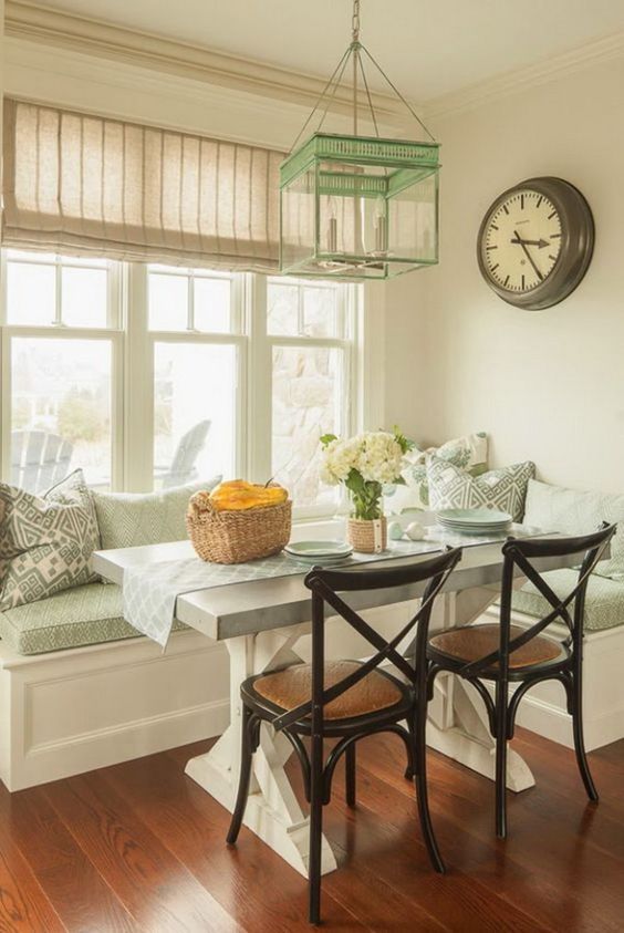 a watercolor cottage-style breakfast nook with rustic accents, a rustic table, black chairs and some printed pillows, and a mint green pendant lamp