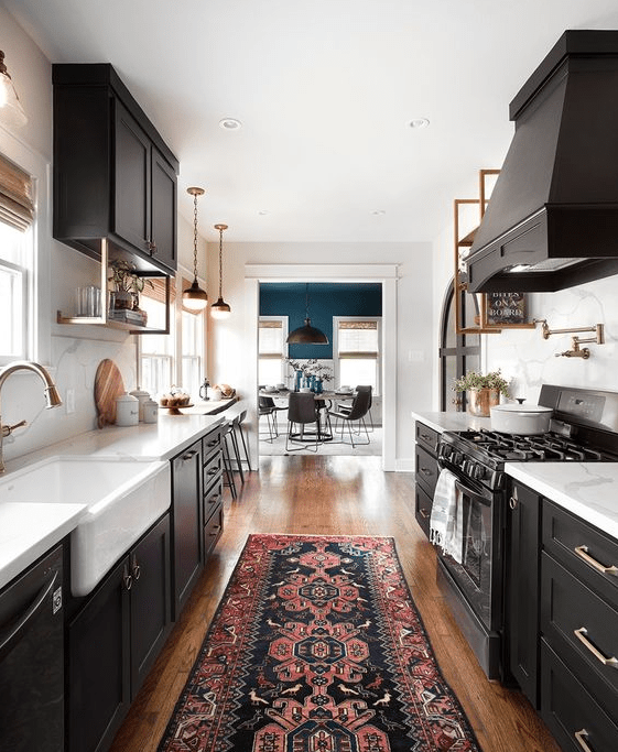 a black galley kitchen with white stone countertops and elegant brass accents here and there