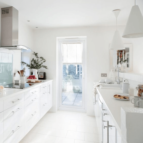 a modern white pantry kitchen with white cabinets, metal and glass elements and access to the terrace with lots of light