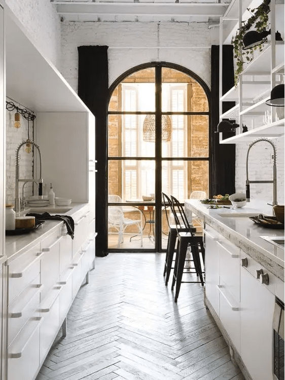 a contrasting galley kitchen with metal cabinets, an arched window, a window dining area and lots of greenery